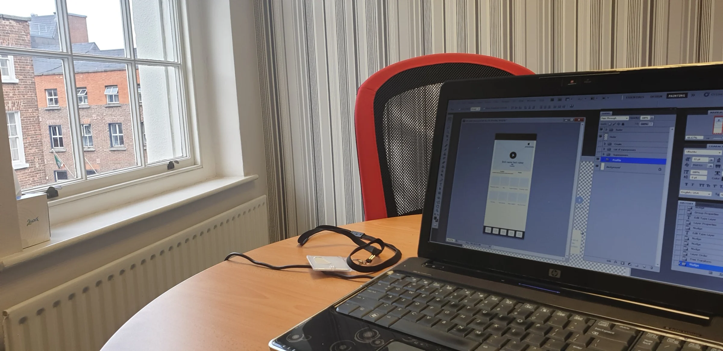 Laptop showing OXYGEAN profile wireframes in Photoshop on a desk by a window